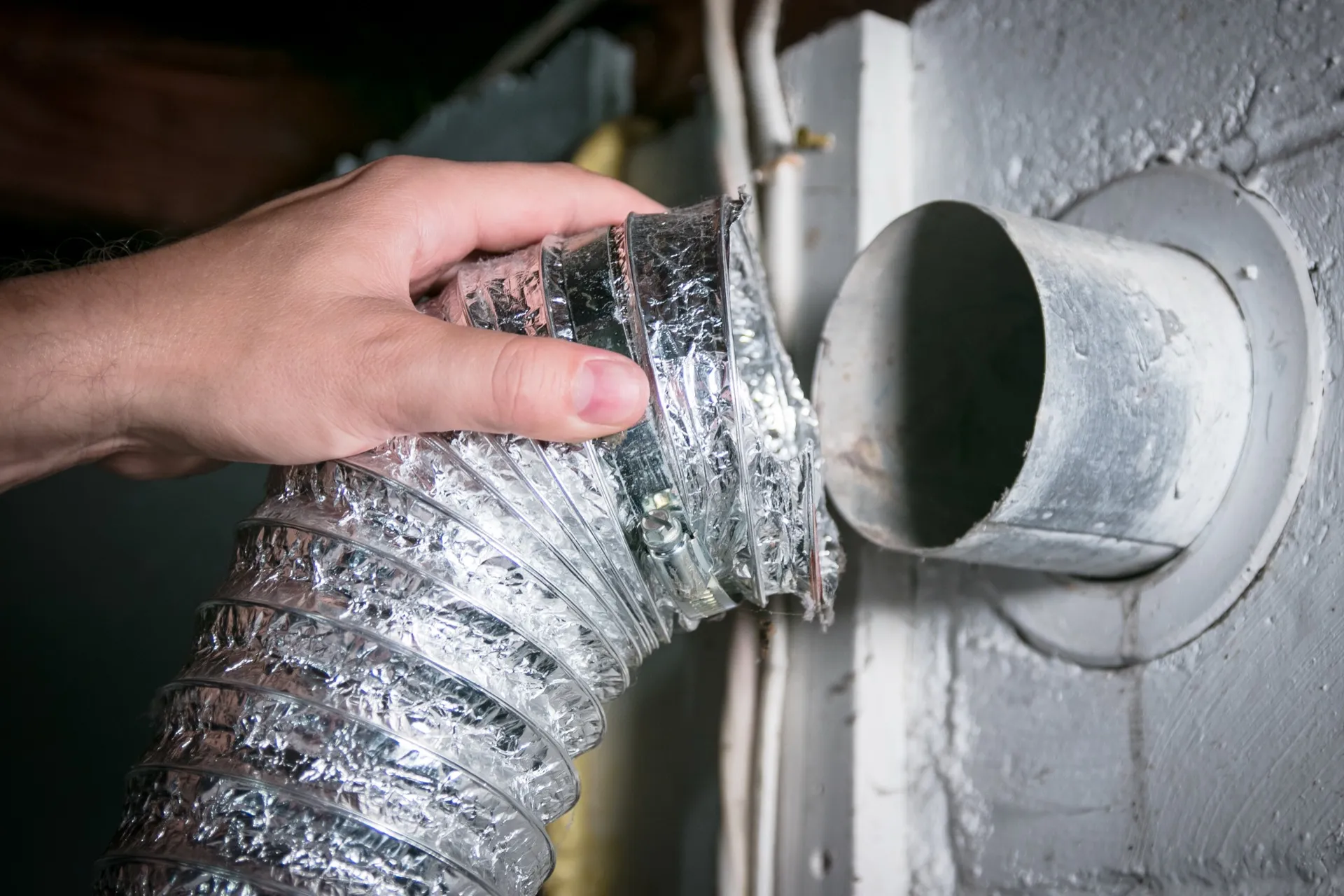 Technician connecting a flexible dryer vent hose to a wall exhaust port