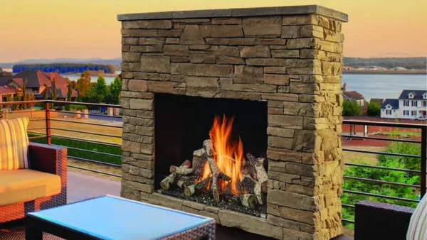 Fire Garden outdoor gas fireplace with a stone surround, burning on a patio at sunset